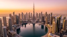 Vue aérienne de Downtown Dubaï au coucher du soleil, avec le Burj Khalifa, un lac réfléchissant et de nombreux gratte-ciel modernes.