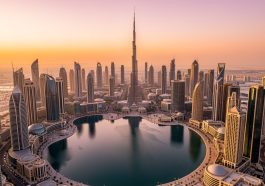 Vue aérienne de Downtown Dubaï au coucher du soleil, avec le Burj Khalifa, un lac réfléchissant et de nombreux gratte-ciel modernes.