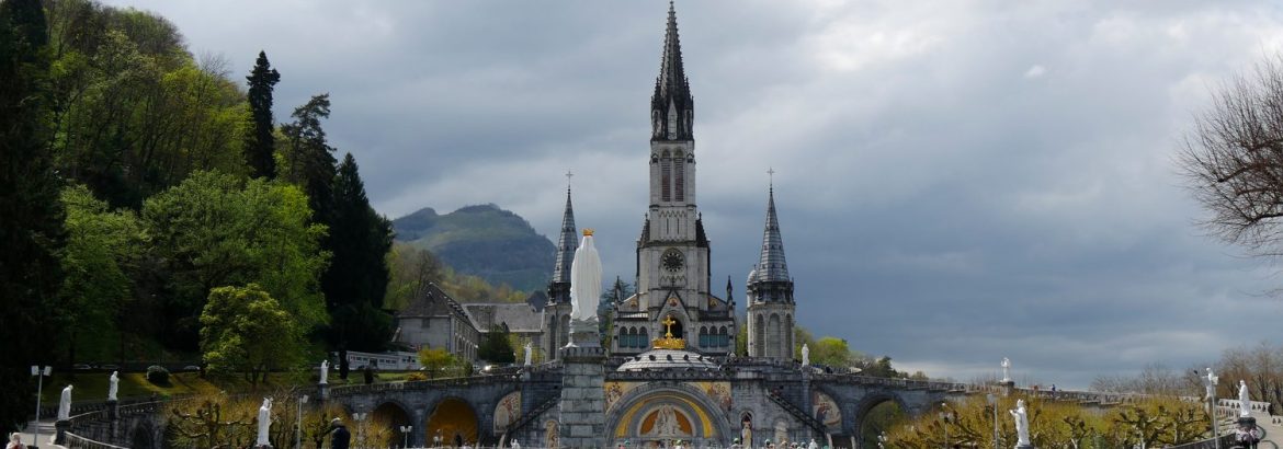 Des pèlerins se recueillent devant le sanctuaire de Lourdes, avec la basilique en arrière-plan.
