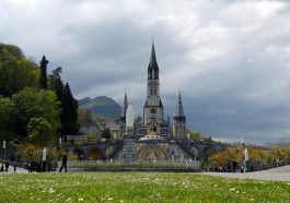 Des pèlerins se recueillent devant le sanctuaire de Lourdes, avec la basilique en arrière-plan.