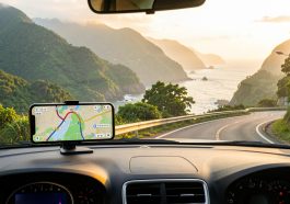 Voiture de location roulant sur une route côtière de Taïwan, avec un smartphone affichant une carte GPS, des montagnes verdoyantes et une lumière matinale.